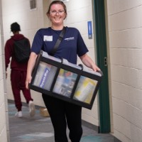 GVSU Alumna smiles as she walks through the dorm hallways carries a box for new Laker